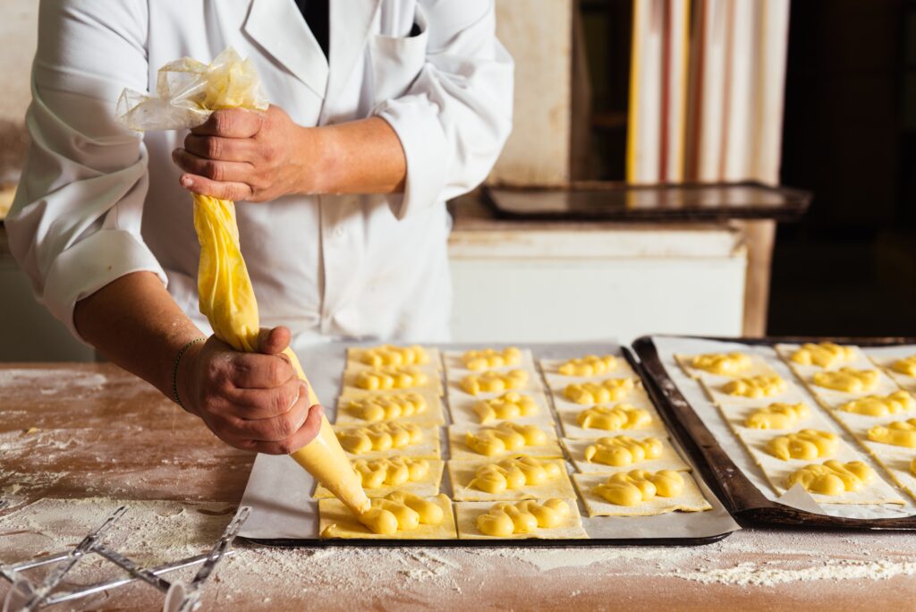 a baker piping cream filling on pastry sheets
